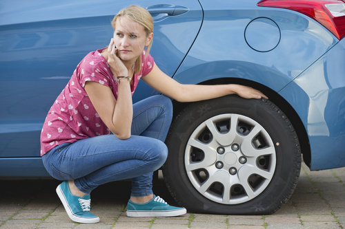 Lady with a flat tire on the phone next to her car